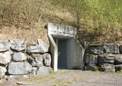 Bunkereingang in einem Hügel mit steinernen Wänden, umgeben von Bäumen und Natur.