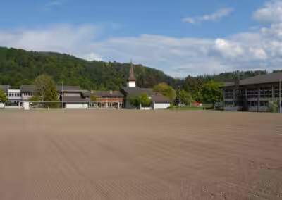 Ländliche Landschaft mit Kirche, Hügeln und Gebäuden, bewölkter Himmel. Ideal für Natur- und Architekturfans.