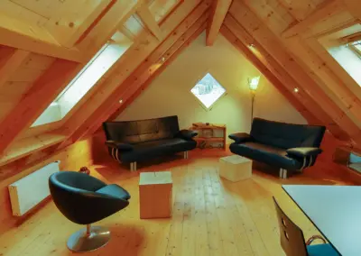 Gemütlicher Dachboden mit Sofas, Drehsessel und Holzboden, ideal für Entspannung und Geselligkeit unter Holzbalkendecke.