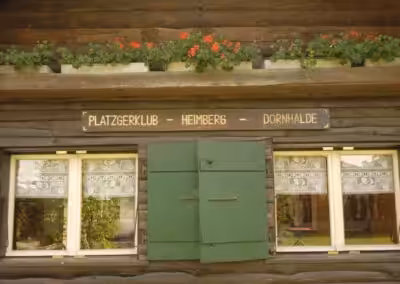 Holzhütte mit Blumenkästen und Fensterläden. Schild: Platzgerklub Heimberg Dornhalde.