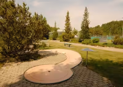 Minigolfplatz im Grünen mit steiniger Bahn und Bäumen im Hintergrund an einem sonnigen Tag.