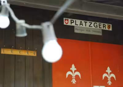 Platzger Klub Heimberg Schild und Tür mit Lilienmotiv, im Vordergrund Girlande mit Glühbirnen.