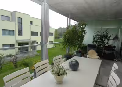 Moderne Terrasse mit Essbereich, umgeben von Pflanzen, mit Aussicht auf das grüne Hofgelände und ein Mehrfamilienhaus.