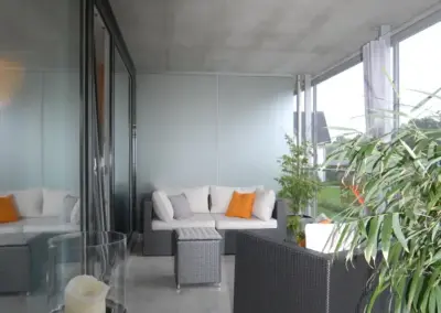 Moderne Veranda mit gemütlichen Gartenmöbeln, orangefarbenen Kissen und Pflanzen, ideal zum Entspannen.